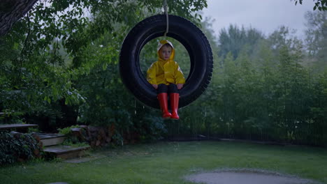 child in yellow raincoat on tire swing in the rain