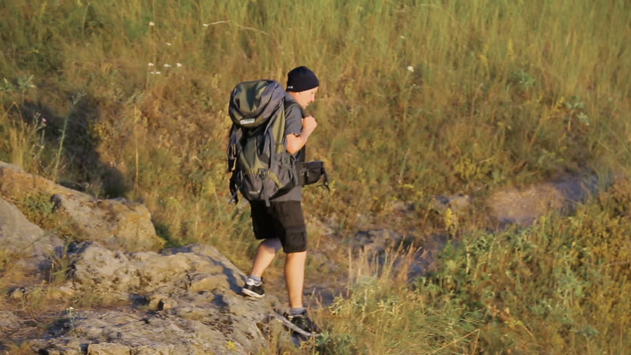 Man Traveling With Backpack. Adult travel man going on the hill near river with backpack