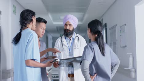 diverse doctors and nurses using tablet and talking in corridor at hospital, in slow motion