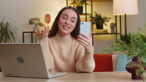 young woman having a video call on her phone while working at home