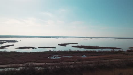 Los-Coches-Circulan-Uno-Tras-Otro-Por-La-Carretera,-Con-Agua-Y-Tierra-A-Los-Lados