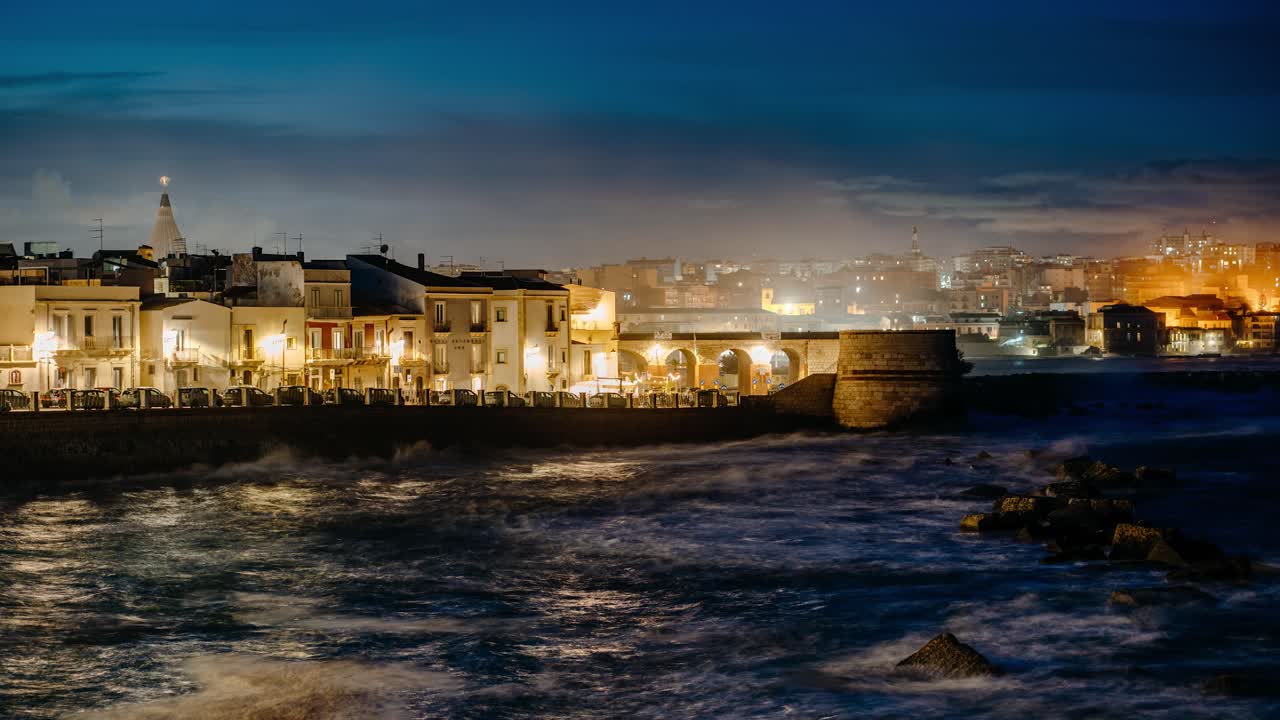 Timelapse of a city by the Mediterranean sea in Italy. Ortigia island at night with waves crashing on the coast. Sicily landscape.