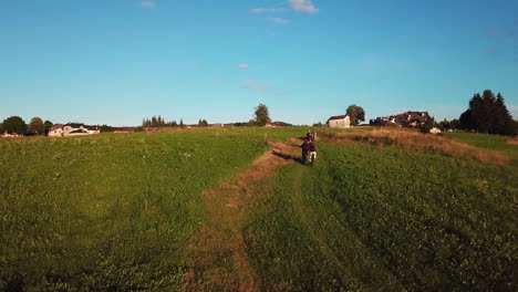 following aerial shot of three mountain bikers driving uphill towards small countryside village in italy