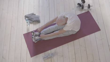 old man using a stretching band and exercising on yoga mat at home 1