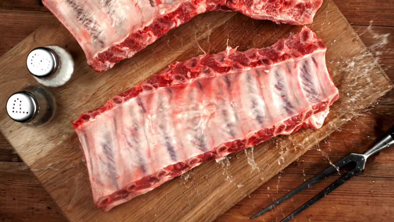 Water Splashing on Raw Pork Ribs on a Wooden Cutting Board