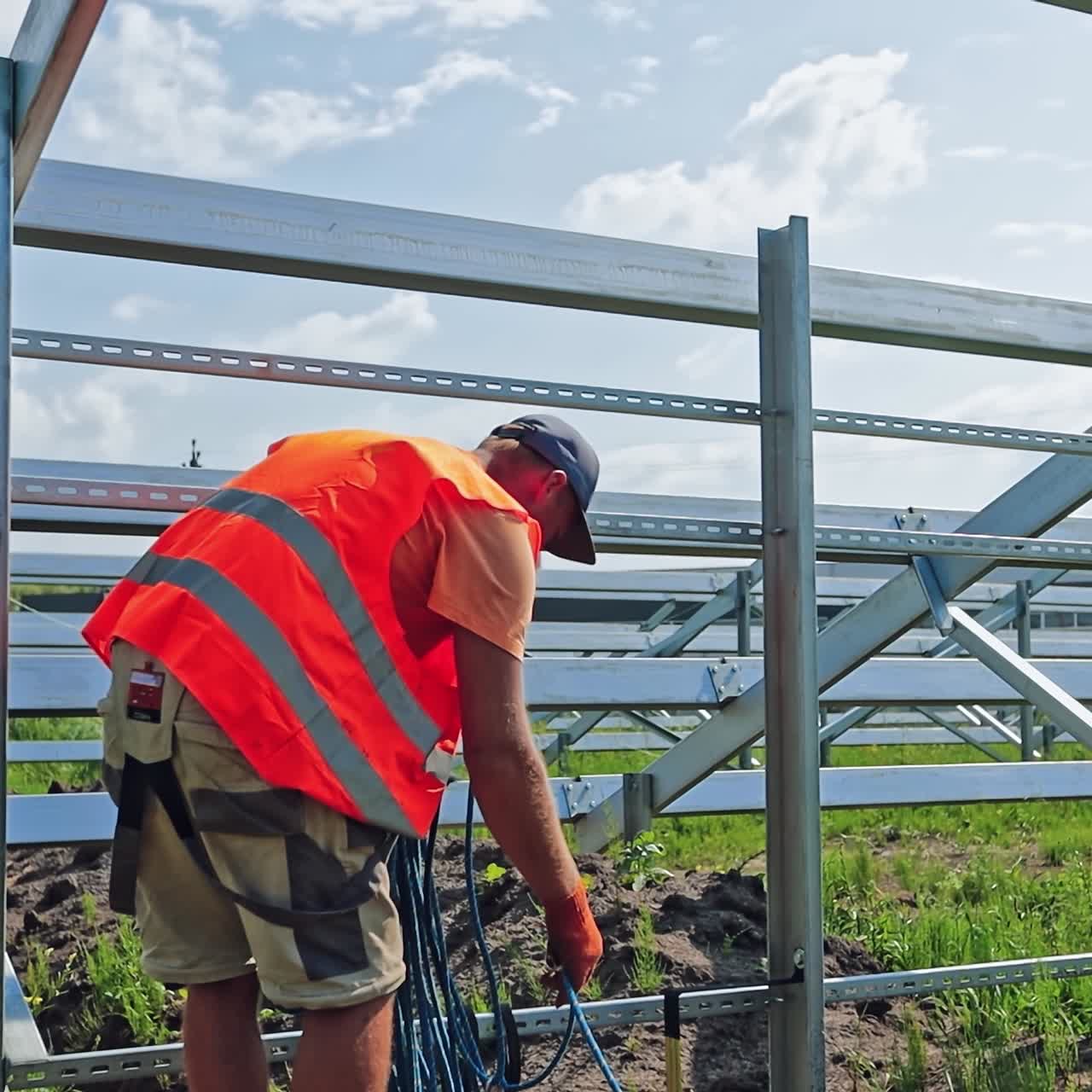 Technician with wires on the solar farm. Worker conducts electrical wire on the field. Solar power plant construction in summer.