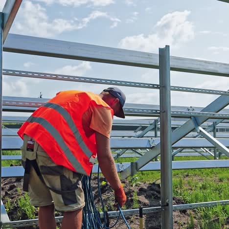 technician with wires on the solar farm. worker conducts electrical wire on the field. solar power plant construction in summer.
