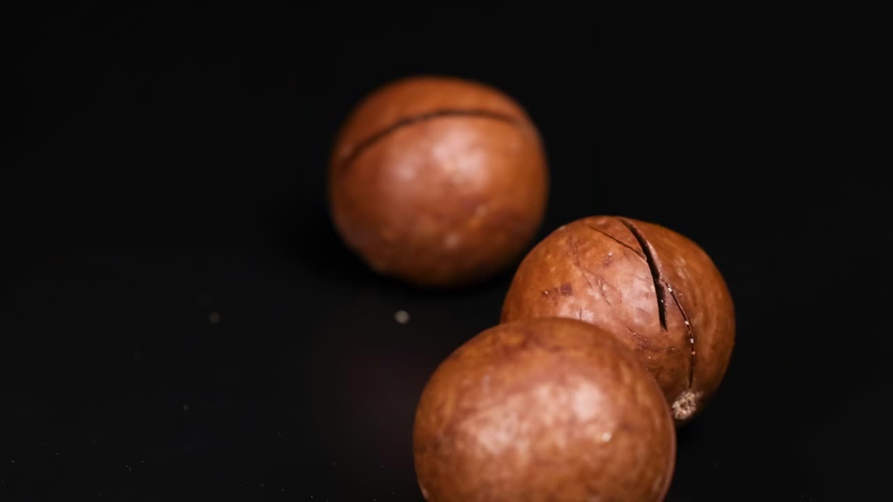 Close-up of hands arranging and touching macadamia nuts on a dark background, highlighting their texture and round shape.