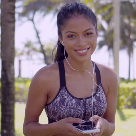 Smiling-Asian-woman-in-earphones-with-smartphone-in-hand-in-park