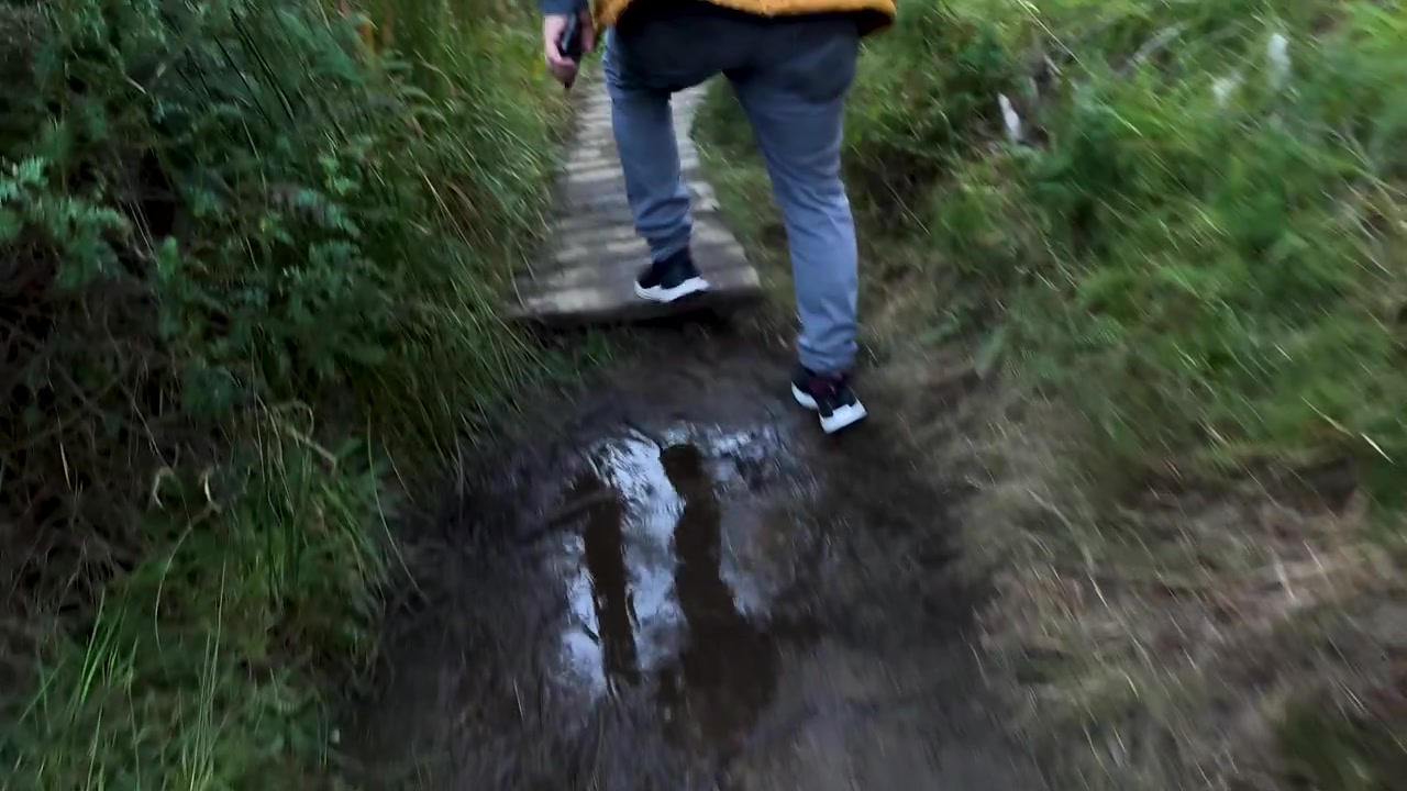 Ripresa dal basso che segue un escursionista che cammina su sentiero fangoso e passerella a Wentworth Falls