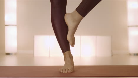 barefoot woman standing on mat in class. woman legs doing tree pose in studio