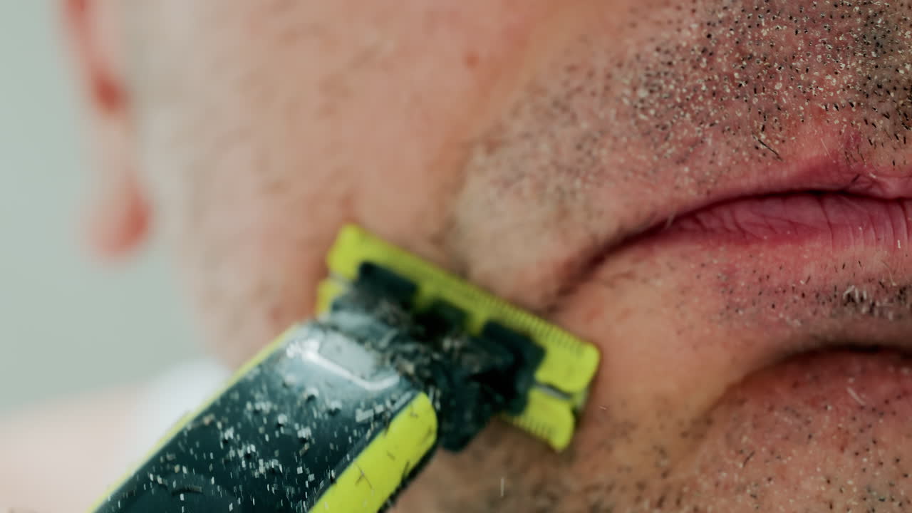 Close up of a man using an electric razor to trim facial hair in the bathroom
