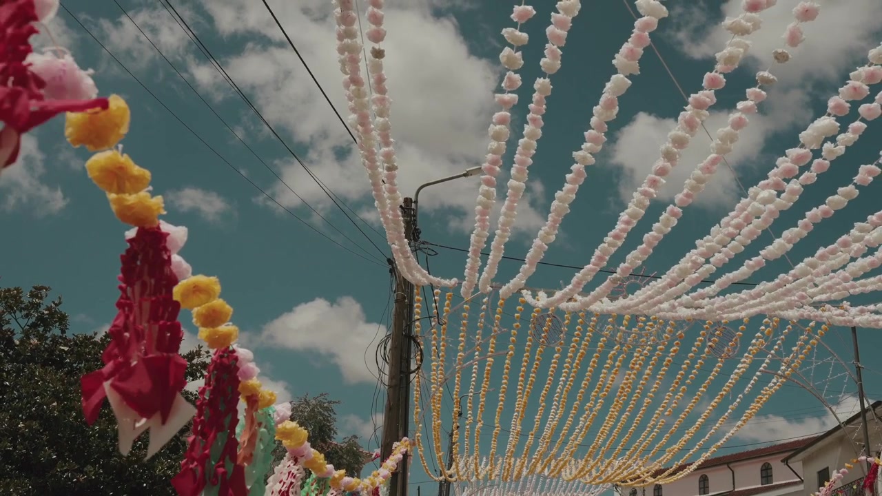 File di festoni di fiori di carta rosa e gialli pendono sopra un palo della strada e le case del villaggio durante il festival di Arraial.