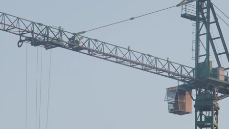 close-up view of a large green construction crane towering against a clear blue sky, highlighting the crane's boom, operator's cabin, and intricate cable system