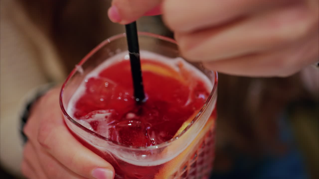 Close up of a woman mixing a red cocktail with a black straw