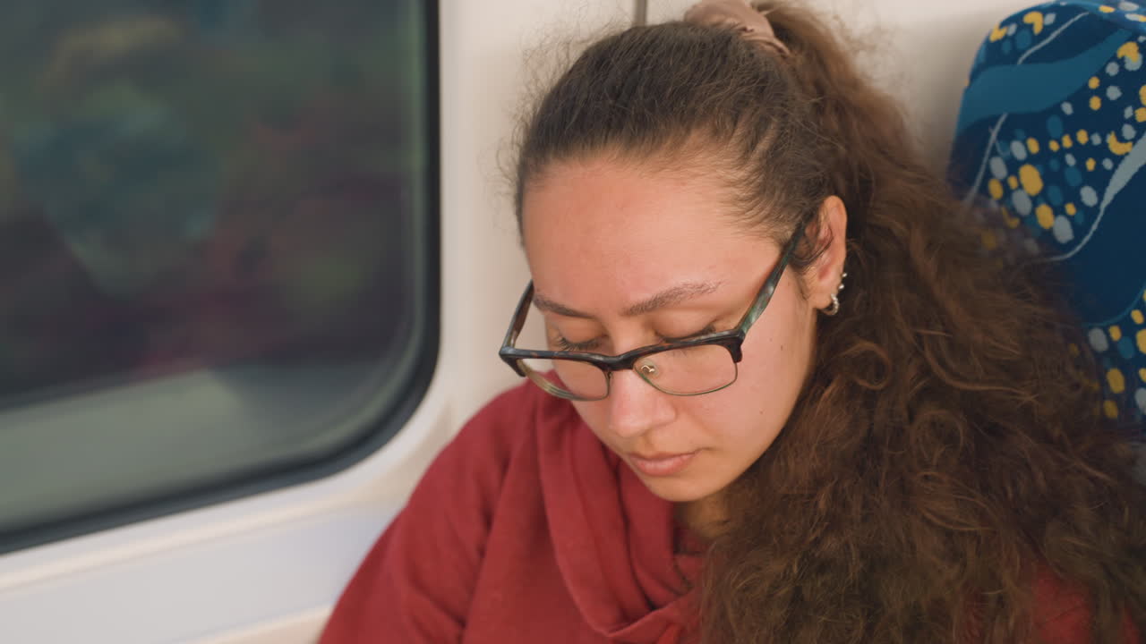 Viaggiatrice urbana che si aggiusta l'auricolare all'interno del treno. Donna in felpa con cappuccio al finestrino che riflette durante il viaggio in treno. Giovane passeggera in abiti casual che guarda pensierosa con la vista della città all'esterno.