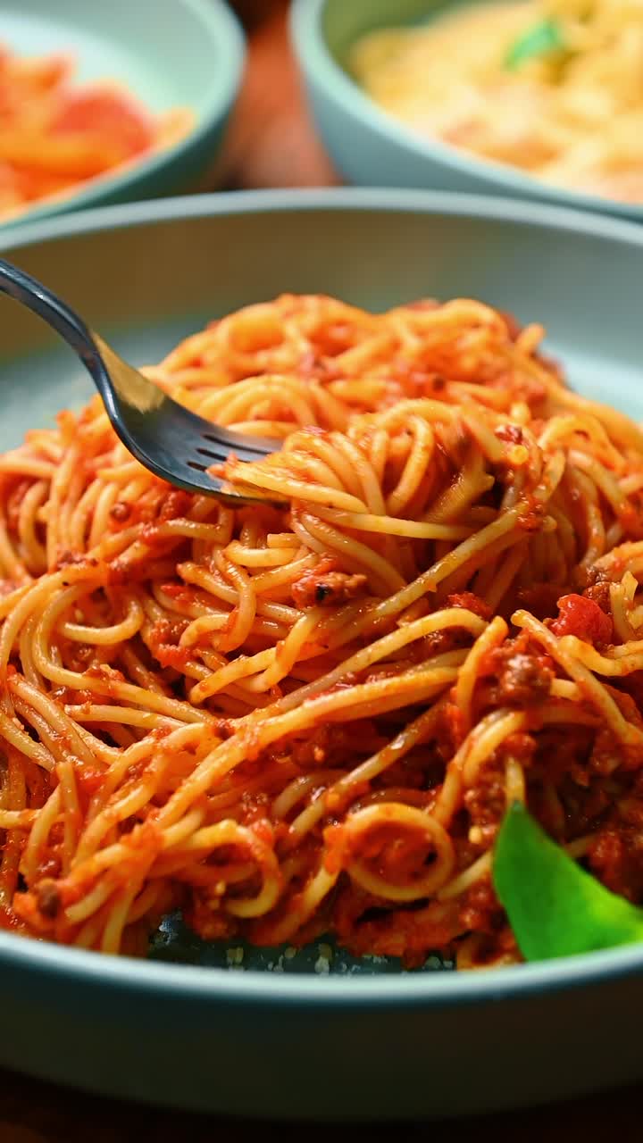 Primo piano di una forchetta che avvolge spaghetti con ragù alla bolognese. Scatto ravvicinato verticale di pasta con salsa di pomodoro rossa, carne macinata e basilico su piatto blu.