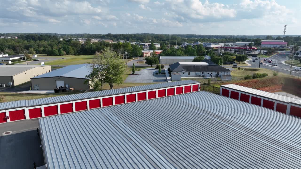 Traffic scene on suburb road near mall and warehouse in america. Drone rising wide shot. Red Garages of rental self storage units with red doors