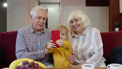 Pareja-De-Ancianos-Abuelos-Con-Nieta-Infantil-Haciendo-Fotos-Selfie-Juntos-En-El-Teléfono-Móvil