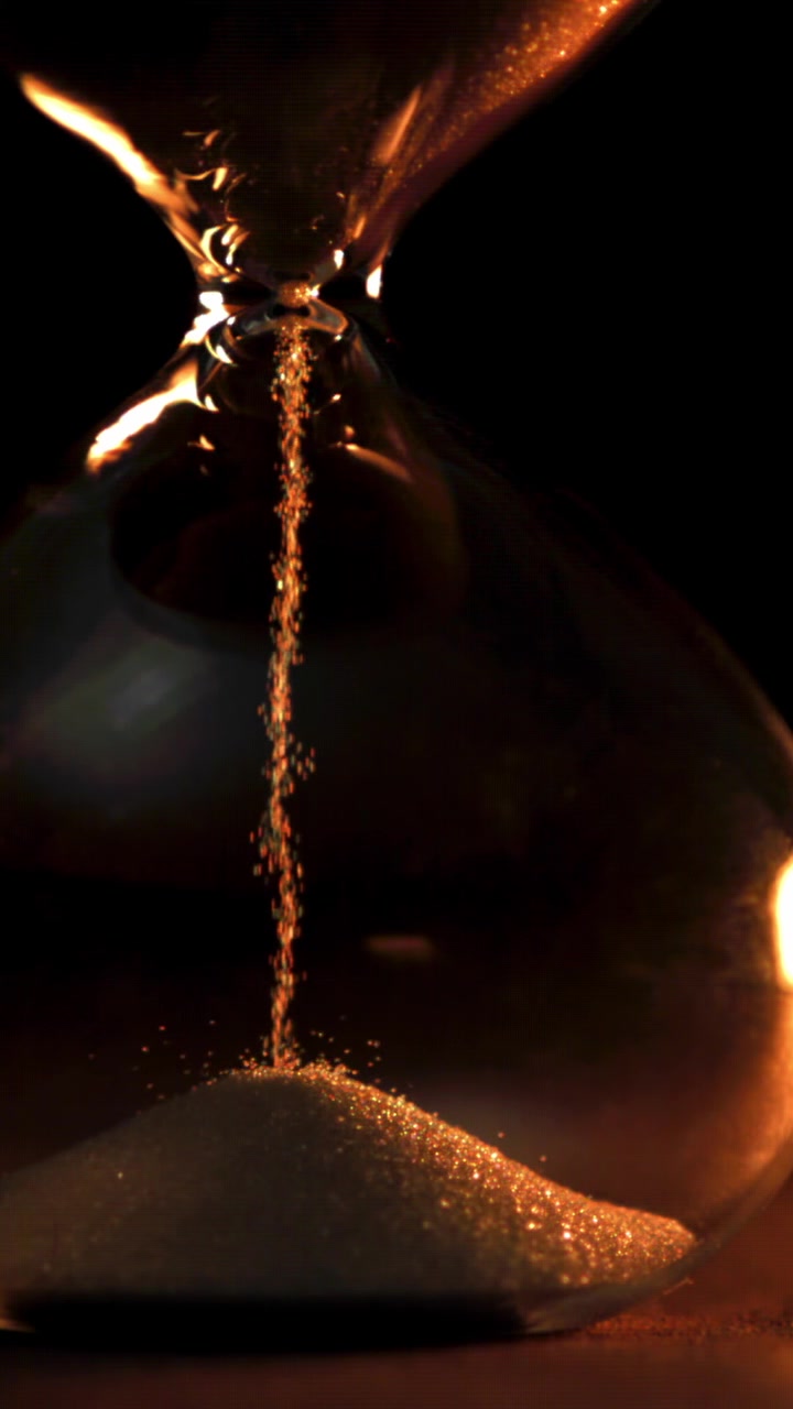 Hourglass with Golden Sand Flowing on Dark Background