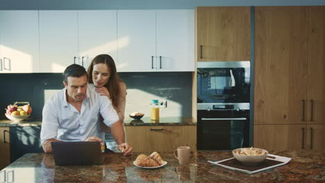 concentrated man working at luxury kitchen. smiling wife talking with husband