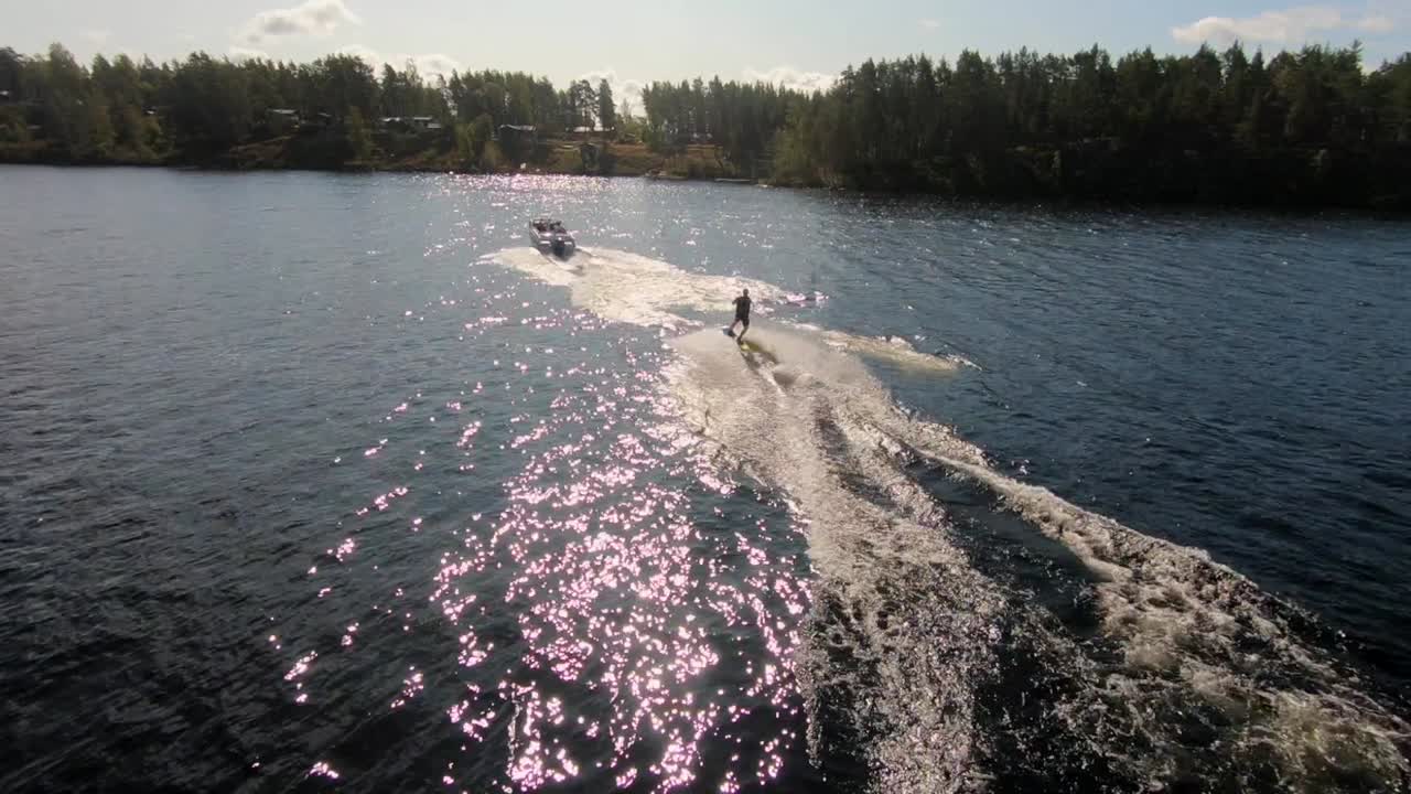 Riprese aeree con drone di un giovane che si alza su una tavola da wakeboard dietro una barca sportiva nell'arcipelago svedese in estate sub6