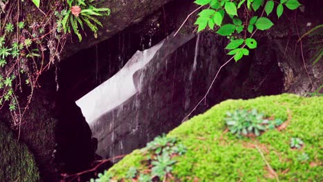 nature left to its own devices, water flows over rocks and behind a small natural window formed by stones