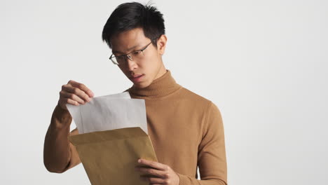 아시아인 남자가 봉투를 열고 내용을 읽고 있습니다.
