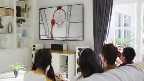 Composite-of-happy-family-sitting-at-home-together-watching-basketball-game-on-tv