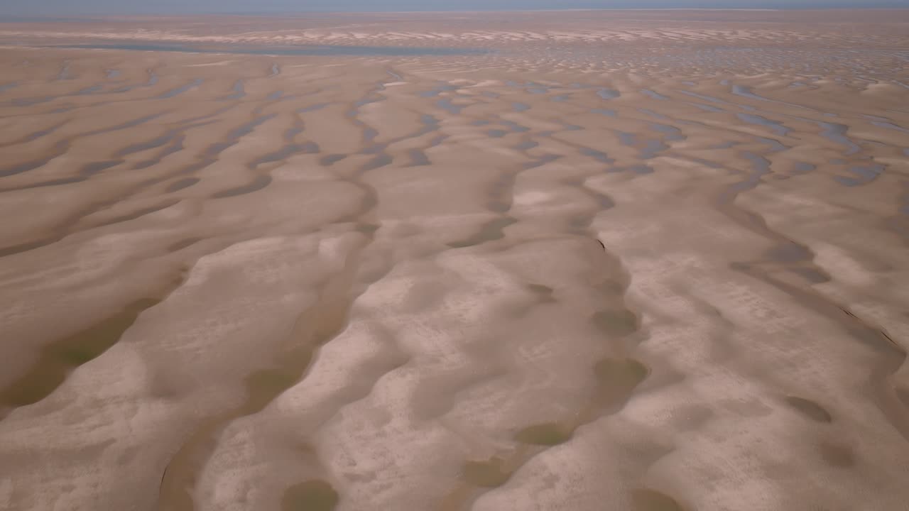 Flying over empty clean tidal sands and seawater pools towards empty horizon on a sunny day. Fleetwood, Lancashire, UK.