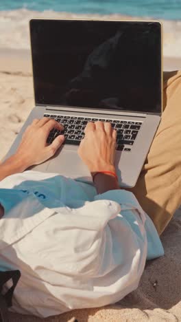 close up hands man freelancer using laptop lying on beach and working remotely