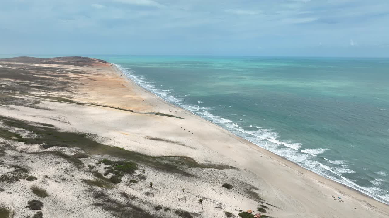 Expansive aerial of sweeping sandy beach, turquoise water, and dry coastal terrain at Jericoacoara, Ceará, Brazil. Bird's eye aerial view