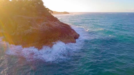 Vista-Aérea-De-Un-Acantilado-Rocoso-Y-Olas-De-Agua-Azul-Turquesa-Salpicando-Al-Atardecer