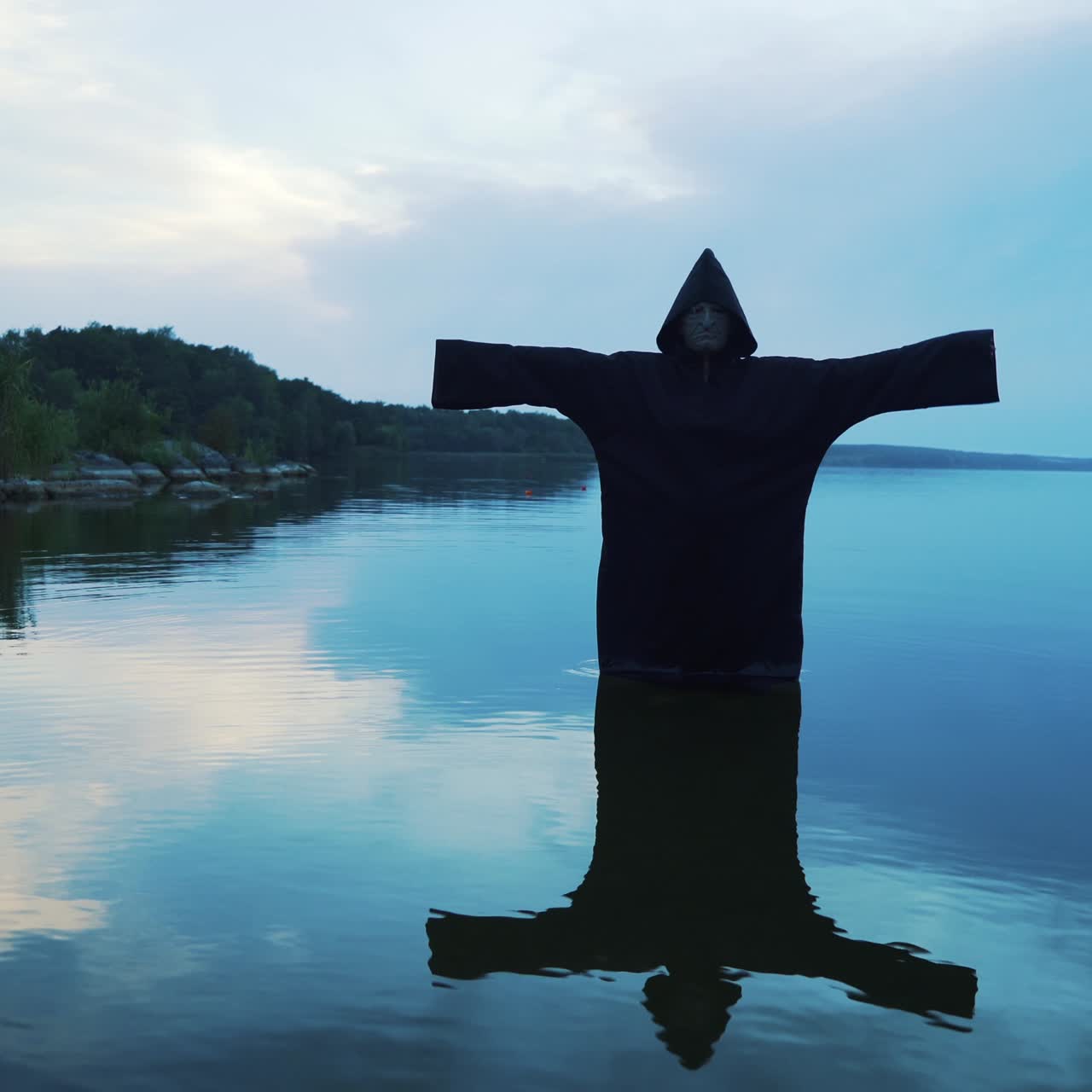 Evil witch in black cloak with hood in the river. Halloween costume.