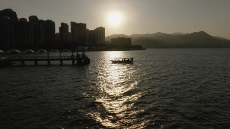 A-low-altitude-drone-shot-over-a-boat-approaching-a-peer-on-the-river-in-Hong-Kong-at-sunset