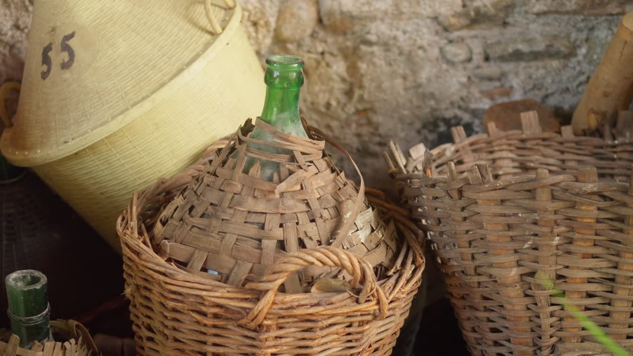 Zblízka: vintage skleněný demižon na víno uvnitř ochranného proutěného koše v tradičním vinařství.