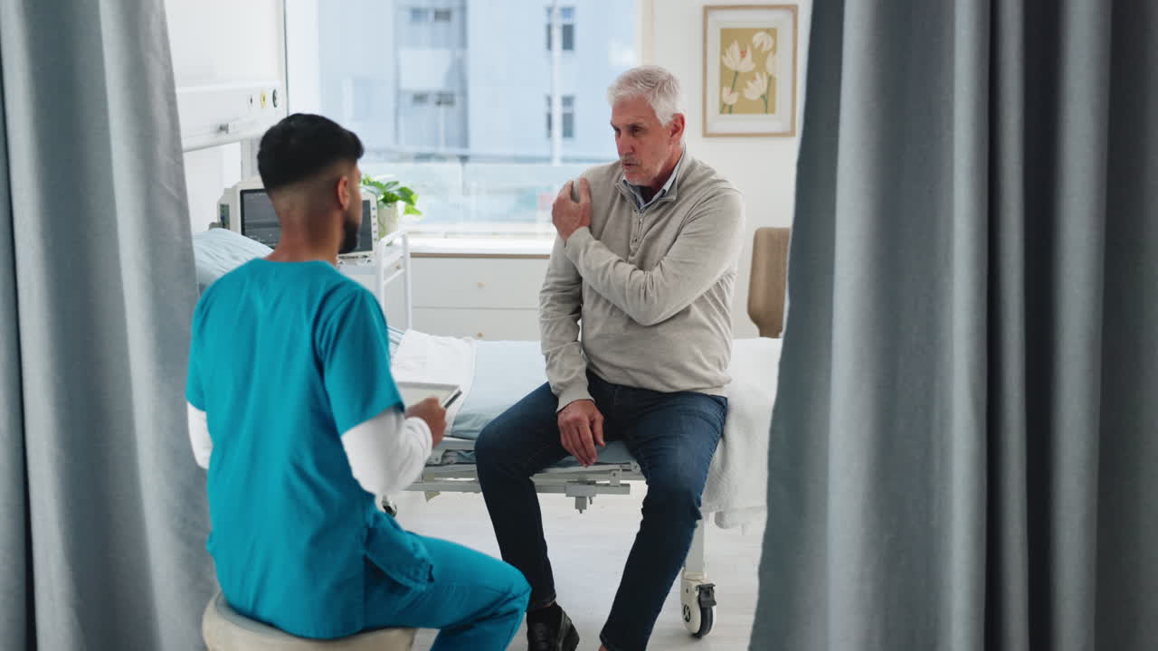 Mannlig pasient diskuterer skuldersmerter med lege på sykehusrom