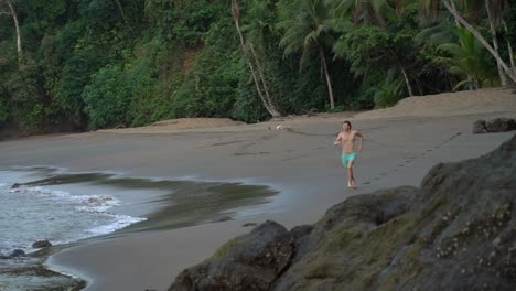 young men running towards camera at sandy beach with pacific and rainforest in the background