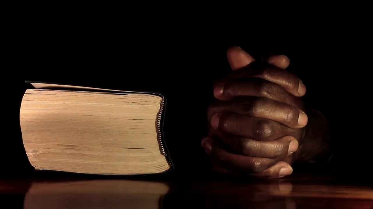 rezando a dios con las manos junto con el hombre caribeño de la biblia rezando con fondo negro almacen de video