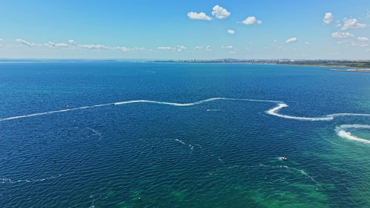 Gara di moto d'acqua in acque aperte in una giornata di sole vicino a una costa con lo skyline di una città in lontananza.