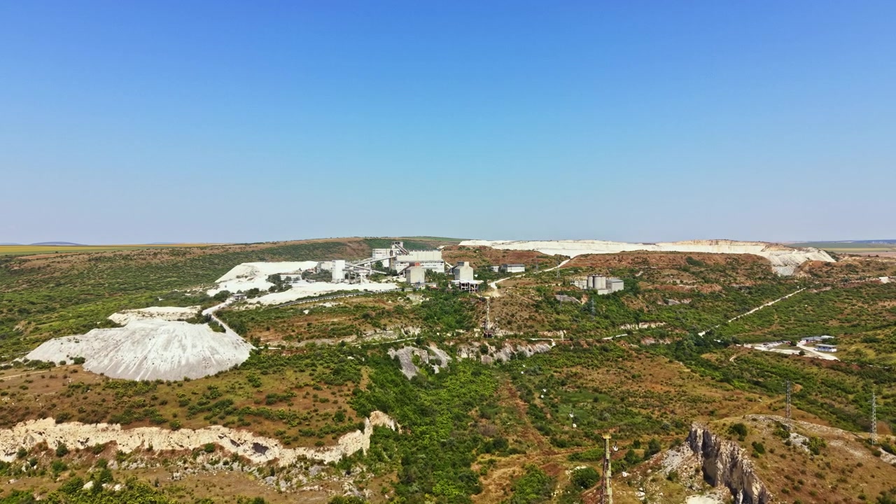 View of a mining site surrounded by green hills under a clear blue sky in a remote area during daytime