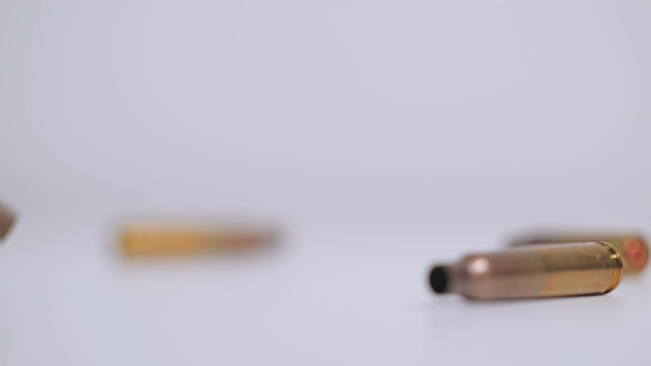 Detailed slow motion of empty bullet casings spinning and falling on clean white