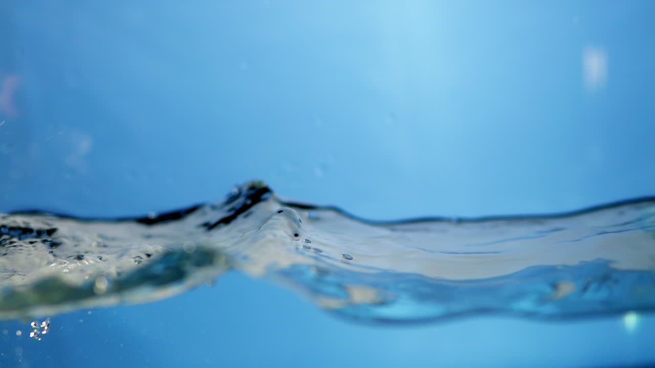 Waves of clear water splattering and creating tiny droplets as it ripples inside a container