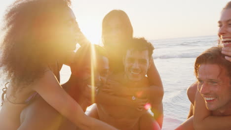 portrait of men giving women piggyback on summer beach vacation