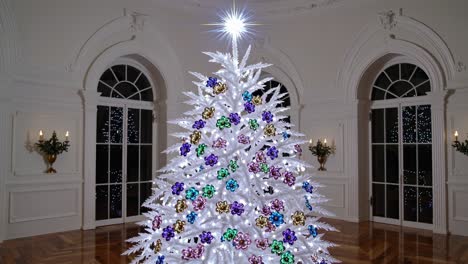 festive white christmas tree glowing with colorful ornaments and lights, standing in elegant room with arched windows creating magical holiday atmosphere