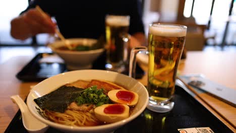 two people sharing a meal of ramen and beer