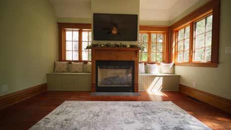 wide push in of a sun room with sunlight beaming through the window showing a tv, fireplace, and 2 bench seating areas