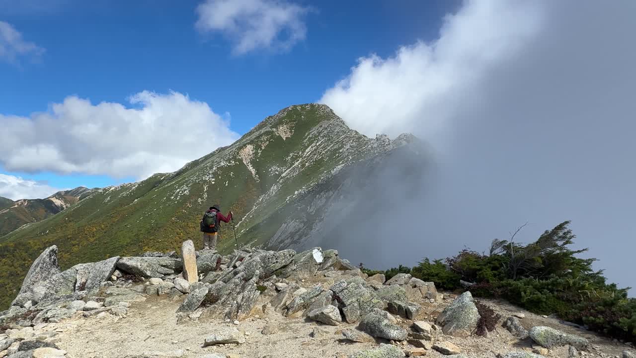 Explore the rugged terrain of Hotaka's mountain ridge in Nagano, showcasing a sweeping view of the Northern Japanese Alps with dramatic clouds and clear skies, perfect for hiking enthusiasts
