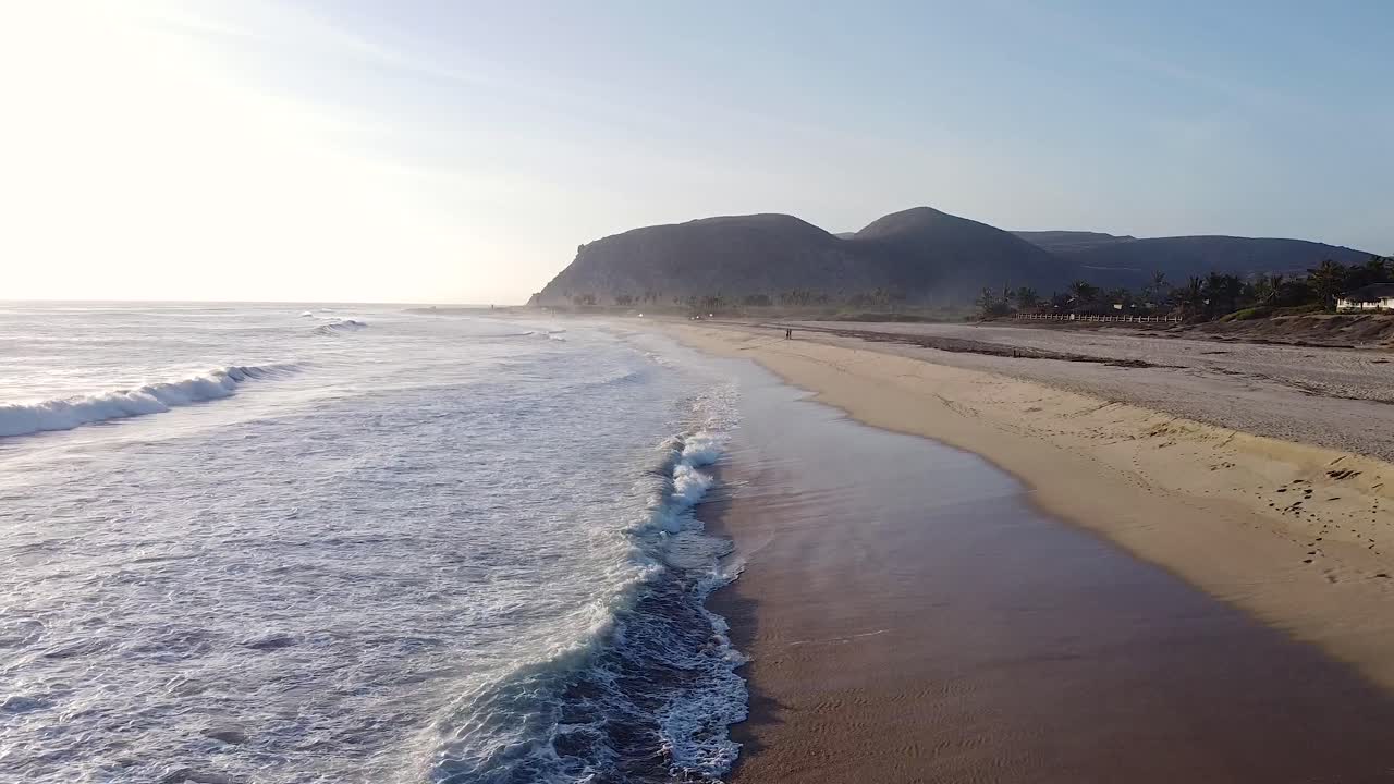cerca de las olas y la niebla del océano chocando contra la playa de arena durante la hora dorada puesta de sol con sobrevuelo de drones