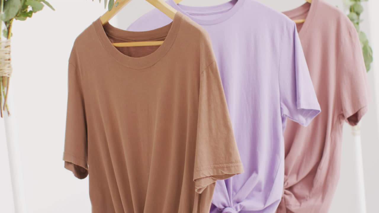 video de primer plano de camisetas blancas, beige y púrpuras colgando sobre un fondo blanco